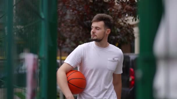 自信的白人男子以慢动作进入户外球场 一个英俊的年轻运动员的画像 他在城市的户外带着篮球走了 健康的生活方式和培训 — 图库视频影像