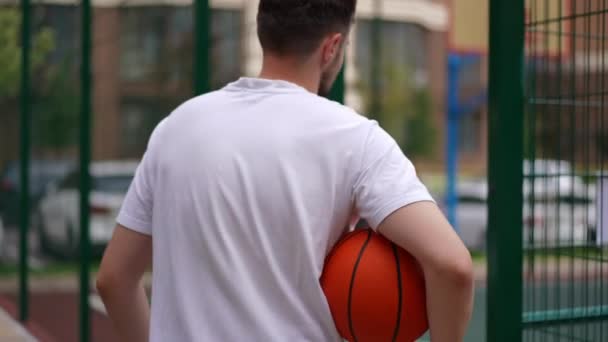 フィットの追跡ショットスローモーションでバスケットボールをプレイ都市スポーツグラウンドに入る白人スポーツマン 屋外でハンサムな若い男の訓練 健康的なライフスタイルのコンセプト — ストック動画