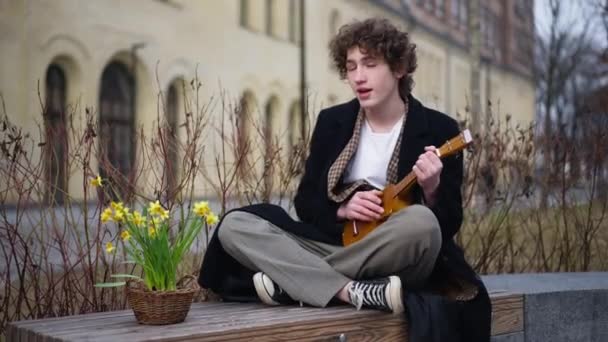 Yetenekli Genç Adam Gitar Çalarak Şarkı Söylüyor Sarı Saksıyla Bankta — Stok video
