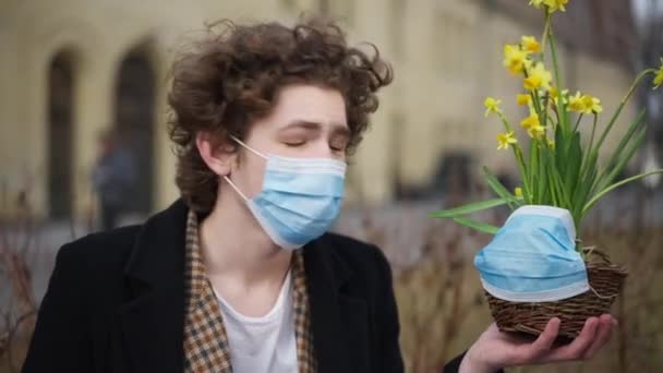 コロナウイルスの白人男性と花の鍋は 街の通りの屋外マスクに直面しています 若いです悲しいです男とともに植物見ますカメラポーズ — ストック動画