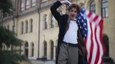 Şehir caddesinde Amerikan bayrağı taşıyan mutlu genç adam gülümseyen kameraya bakıyor. Ulusal sembolü açık havada poz veren heyecanlı neşeli adamın portresi.