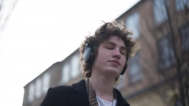 Поглощенный Молодой Человек Слушающий Музыку Снимающую Наушники Глядя Улыбающуюся Камеру — стоковое видео