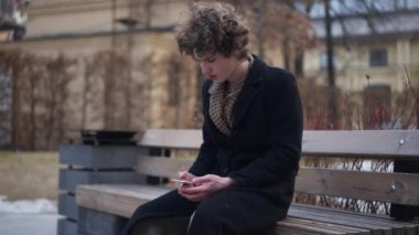 Sorunlu genç yakışıklı adam kenarda oturmuş internetten mesajlaşıp başka tarafa bakıyor. Tereddüt eden Kafkasyalı zarif adamın portresi açık hava telefon uygulamasında internette sörf yapıyor.