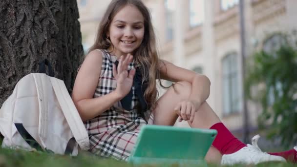 デジタルタブレット上のビデオ通話アプリを使用して話を振って魅力的な喜びの女の子 笑顔の肖像画幸せな白人女子高生メッセージングオンライン座っている学校の庭 — ストック動画
