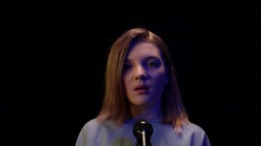 Elinde mikrofonla kameraya bakıp ışığı kapatan kendine güvenen bir kızın portresi. Sahnede karanlıkta poz veren Kafkasyalı ergen sanatçı.