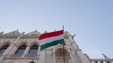 Budapeşte, Macaristan - 16 Mayıs 2022: Macaristan Parlamento Binası 'nda ulusal bayrak dalgalanıyor. Şehir caddesindeki Gotik kalede milli kimlik sembolünün alt açısı