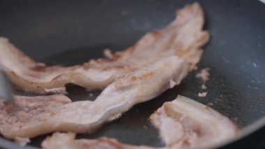 Domuz pastırmasını çatalla kızartma tavasına yakın plan çevirme. Tanımlanamayan beyaz adam evde lezzetli et pişiriyor. Mutfak ve yaşam tarzı kavramı
