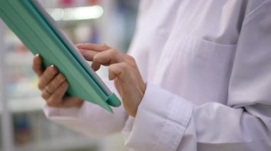 Tanınmayan beyaz kadın eczanede yavaş çekimde dijital tablet dokunmatik ekranı kaydırıyor. Akıllı kendine güvenen çalışan eczanede siparişleri kontrol ediyor.