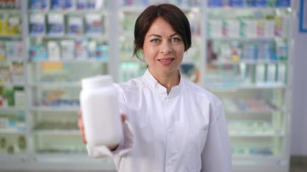 カメラの笑顔を見て丸薬の肯定的な自信の女性の瓶ストレッチ フロントビュー薬店で効率的な薬でスローモーションでポーズ白人女性薬剤師 — ストック動画
