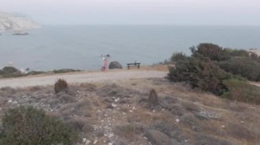Akdeniz 'de geniş bir uçurum ve peri kostümlü beyaz bir kadın keman çalıyor. Kıbrıs 'ta bulutlu bir günde yetenekli kendine güvenen sanatçının açık havada performans sergilediği yüksek açılı manzara