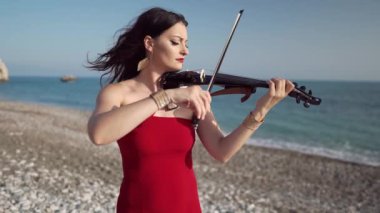 Kıbrıs 'ta Akdeniz sahilinde keman çalan yetenekli bir kadının yan görünümü. Kendine güvenen güzel bir sanatçı. Sahilde gün ışığında müziğin tadını çıkarıyor.