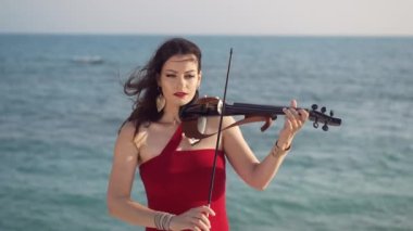 Günışığında mavi Akdeniz dalgalarının arka planında keman çalan kendine güvenen bir kadından esinlendim. Açık havada müzikten hoşlanan beyaz bir kadının orta boy portresi.