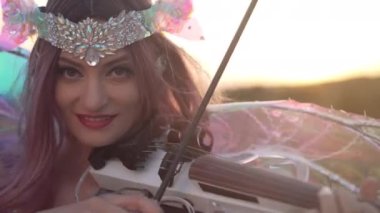 Gün batımında dağlarda keman çalan gülümseyen kadın. Kendine güvenen beyaz müzisyenin portresi. Açık havada gün ışığında müzik yapıyor.