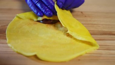 Yakından çekilen el yapımı böğürtlen ve çikolatalı krema yavaş çekimde gidiyor. Eldivenli tanınmayan bir kadın içeride lezzetli yemekler yapıyor.