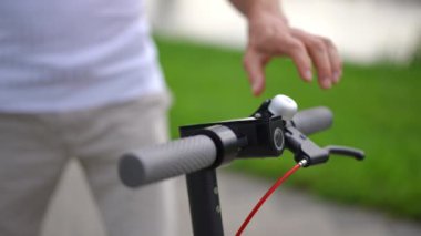 Yakın çekim erkek elleri yavaş çekimde elektrikli scooterın direksiyonunu tutuyor. Tanımlanamayan beyaz bir adam dışarıda araç sürüyor.