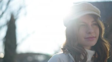 Esmer, beyaz, kahverengi gözlü, açık havada ağır çekimde poz veren genç bir kadın. Kendine güvenen gülümseyen bir kadının yakın plan portresi. Güneş ışınlarında duran kameraya bakıyor.