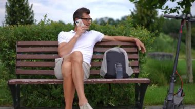 Ön görüş geniş, telefonda ağır çekimde konuşan ciddi bir adam dışarıda bankta oturuyor. Beyaz adamın portresi. Bahar günü parkta sohbet eden rahat bir adam.