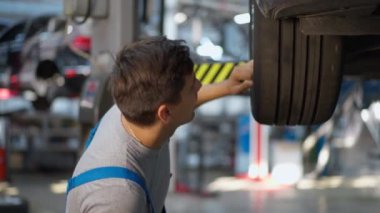 Yan görüş, kapalı alanda araba lastiklerini inceleyen beyaz, yakışıklı bir adam. Odaklanmış uzman bakım mühendisi servis istasyonunda otomobil tamir ediyor.
