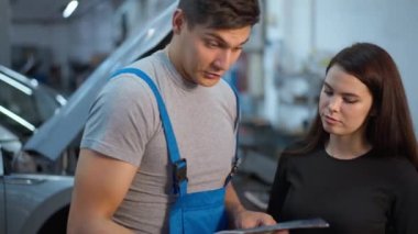 Uzman beyaz adam otomobil servis istasyonunda genç bir kadınla konuşuyor. Evrak gösteriyor. Kendine güvenen bakım mühendisinin portresi.