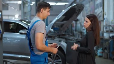 Benzin istasyonunda adamla tartışan hoşnutsuz bir kadın. Beyaz kadın müşterinin erkek tamirciyle tartışırken orta açıdan çekilmiş bir fotoğrafı. Otomobil endüstrisi kavramı