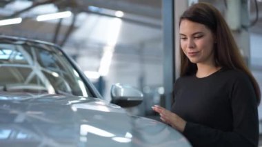 Güzel beyaz bir kadının portresi araba kaputuna dokunuyor gülümsüyor ve galeride araç seçiyor. Kendine güveni tam, çekici bir alıcı içeride yeni bir araba almaya karar veriyor.