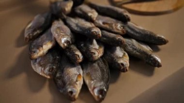 Masaya yakın çekimde kurutulmuş balık ve erkek eli yığının üzerine daha çok koyuyor. Eldivenli, tanınmayan beyaz adam içeride lezzetli yemekler hazırlıyor.