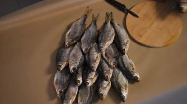 Yüksek açılı manzara, masadaki kurutulmuş balığa yakınlaşır. Erkek eli eldivenli, lezzetli atıştırmalıklar yerleştirir. Tanınmayan bir adam mutfakta lezzetli bir yemek hazırlıyor.