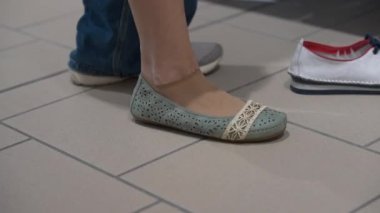 Kapalı zeminde fayanslı bale sahalarında kadın ayağı. Yeni ayakkabılar deneyen beyaz bir kadın. Ayakkabılarını çıkarıyor.