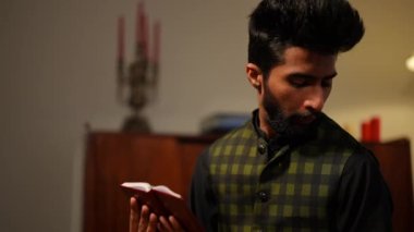 Genç Müslüman adam yan yana tükürüyor ve evde dua ediyor. Ramazan 'da Kuran' a inanan kendinden emin Orta Doğulu erkek portresi