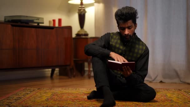 在斋月上坐在右边客厅祈祷的年轻穆斯林男子的画像 中东人阅读 古兰经 期末书的广博前景 — 图库视频影像