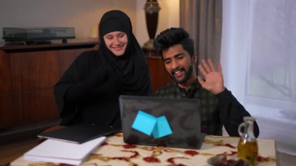 现场摄像头放大到迷人的积极的中东青年男子和白种人在头巾挥动说话使用视频聊天笔记本电脑 快乐的夫妻在家里网上发短信 — 图库视频影像