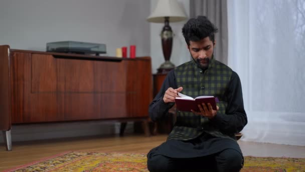 年轻的穆斯林男子跪在客厅的右边 古兰经 他仰起头 向两边吐口水 看完了书 关于斋月的中东信奉者的全景画像 — 图库视频影像