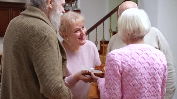 白种人的老夫老妻带着派在家里欢迎几位朋友 带着甜甜的甜食的积极的微笑的男人和女人拥抱客人 永恒的友谊和生活方式 — 图库视频影像