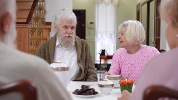 英俊的大胡子老人和白发苍苍的漂亮女人和朋友们坐在桌旁喝茶 轻松的白人丈夫和妻子参加集会的正面画像 — 图库视频影像