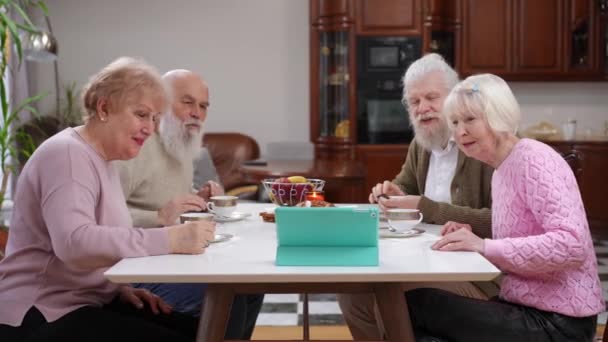 一群积极的老年男女通过茶话会上的数码平板电脑视频聊天 在网上聊天 笑笑白种人朋友享受室内的退休聚会 便利性和生活方式 — 图库视频影像