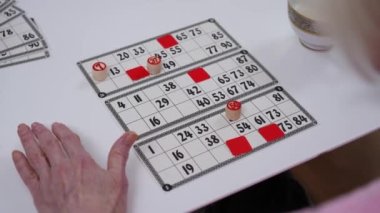 Yüksek açılı loto kartları ve son sınıf bayan el yapımı oyun çipi. Tanımlanamayan Kafkasyalı yaşlı kadın içeride bingo oynuyor.