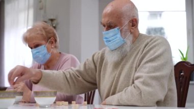 Coronavirus maskeli kıdemli Kafkas karı-koca arkadaşlarıyla masa loto oynuyorlar. İçerde oyundan zevk alan konsantre yaşlı çiftin kenar açılı görüntüsü