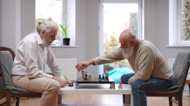 Satrançta eski bir dostla el sıkışarak kazanan zeki, kıdemli, beyaz bir adam. İçeride oyundan zevk alan mutlu, rahat emeklilerin yan görünüm portresi.
