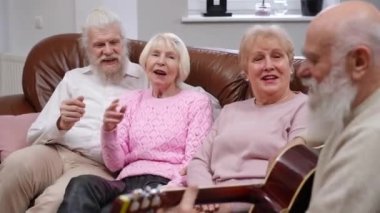 Bir grup rahat kıdemli arkadaş gitar çalan yetenekli sakallı adam olarak şarkı söylüyor. Mutlu Kafkasyalı emekliler içeride eğleniyor.
