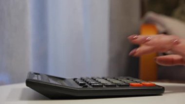 Hesap makinesinin yan görüntüsünde kadın beyaz el tuşlarına basıyor. Kapalı mekanda hesaplama yapan tanınmayan bir kadın.