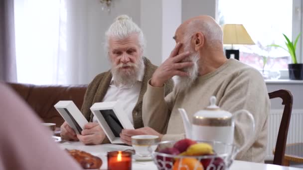 Радостные Бородатые Старики Разговаривают Наблюдая Старыми Фотографиями Сидящими Столом Гостиной — стоковое видео