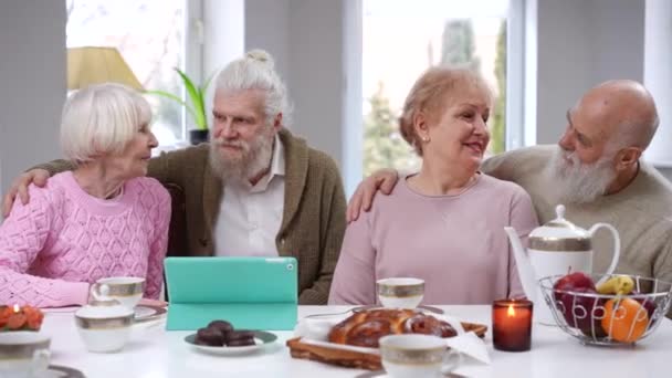 中出し正白人の老夫婦の笑顔とカメラを見て抱擁 フロントビューポートレートのシニア男性と女性のポーズリビングルーム内のテーブルに座って — ストック動画