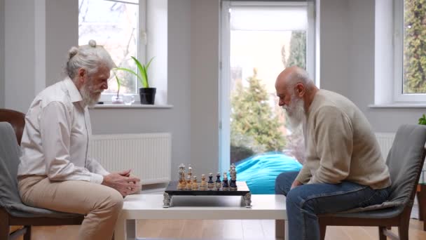 侧面看两个专注的白人老人在屋里想下棋 以男性为重点的资深朋友享受退休游戏 — 图库视频影像