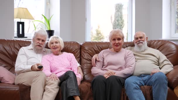 リラックスした退職者のカップルは リビングルームのテレビの話を見ながらソファに座っている 笑顔幸せな屈託のない白人男性と女性週末のレジャーを楽しんで屋内 — ストック動画