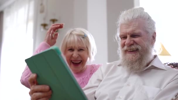 快乐的老夫妇大声笑着观看数字平板电脑上的在线视频 快乐而轻松的白人丈夫和妻子在家里享受着闲暇 — 图库视频影像