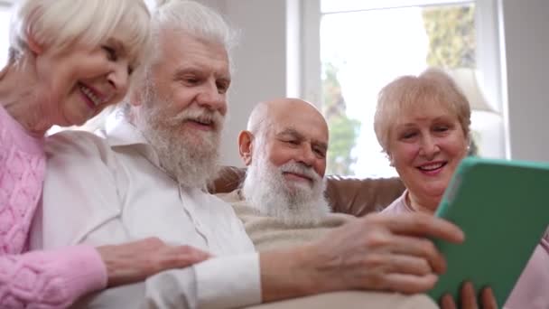 四个轻松 积极的白人男人和女人在网上看电影 谈笑风生 快乐的情侣们坐在客厅的沙发上 坐在数码平板电脑上欣赏喜剧电影 — 图库视频影像