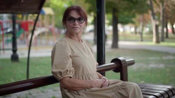 Mulher Madura Confiante Bonita Vestido Sentado Banco Parque Cidade Olhando — Vídeo de Stock