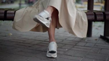 Şehir parkında yetişkin kadın bacakları ve spor ayakkabıları. Ön manzara tanınmayan beyaz kadın bankta oturmuş keyfine bakıyor.