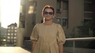 Canlı kamera, kendine güvenen olgun bir kadının güneş ışığında poz vermesini gösteriyor. Güzel, beyaz, kadın, emekli, gün batımında güneş ışığında poz veriyor.