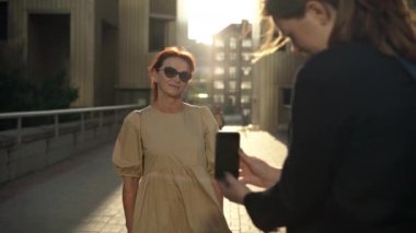 Akıllı telefon uygulaması ile fotoğraf çeken genç bayan kılığına girmiş mutlu bir beyaz kadın. Memnuniyet portresi. Şık, zarif bir büyükanne. Torunuyla şehir merkezinde eğleniyor.